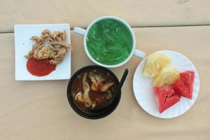 fasting appetizer with sliced fruit, soup, cucumber juice and fried chicken skin photo