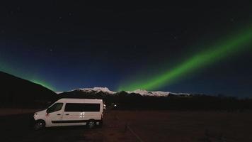 Skaftafell, Iceland, 2023 - Campervan stand on parking in Skaftafell campground with couple watch Aurora northern lights at night over snowy mountain peak in Skaftafell, Iceland video