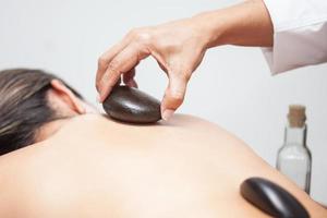 Doctor performing a hot volcanic stones therapy on a young female patient back photo