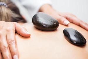 Doctor performing a hot volcanic stones therapy on a young female patient back photo