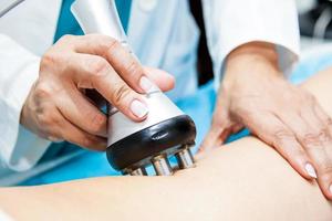 Doctor performing a radiofrequency treatment on a young female patient leg photo