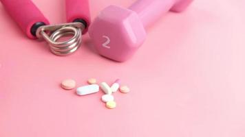 Pink color dumbbell and medical pills on pink background video
