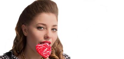 The face of a girl with candy on a stick in the form of a heart on a white background. Sweet woman. photo