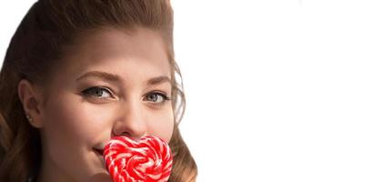 The face of a girl with candy on a stick in the form of a heart on a white background. Sweet woman. photo
