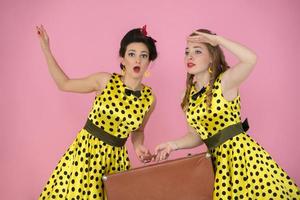 Retro traveler girls with suitcase. Two women dressed in fifties style are holding an old suitcase. photo