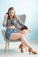Woman in the style of the fifties. Beautiful retro woman with a phone in an armchair. photo