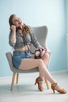 Woman in the style of the fifties. Beautiful retro woman with a phone in an armchair. photo