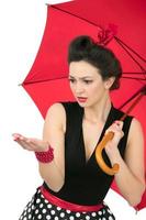 A retro girl pinup with a red umbrella watching the rain. photo