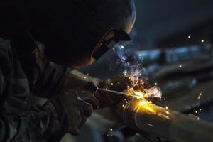 Welder at work. Man in a protective mask. The welder makes seams on the metal. Sparks and smoke when welding. photo