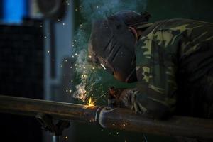 Welder at work. Man in a protective mask. The welder makes seams on the metal. Sparks and smoke when welding. photo