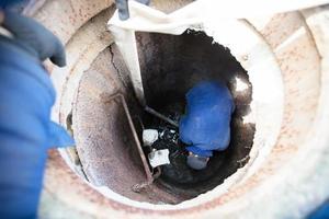 Worker cleans the sewer hatch.A worker cleans a sewer hatch. A man in the hatch. photo