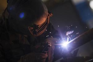 Welder at work. Man in a protective mask. The welder makes seams on the metal. Sparks and smoke when welding. photo