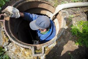 trabajador limpia el alcantarilla escotilla.a trabajador limpia un alcantarilla escotilla. un hombre en el escotilla. foto