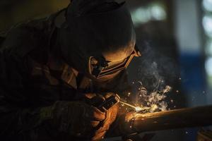 Welder at work. Man in a protective mask. The welder makes seams on the metal. Sparks and smoke when welding. photo
