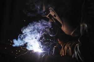 Welder at work. Man in a protective mask. The welder makes seams on the metal. Sparks and smoke when welding. photo