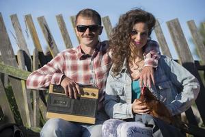 un niña con un pollo y un hombre con un retro magnetófono son sentado en el banco. el aldeanos son en el estilo de el noventa foto