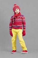 un niño en cálido, brillante ropa. chico en invierno sombrero, bufanda y rojo suéter y zapatillas. de moda chico en el estudio. foto