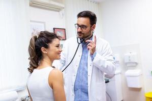 Caring doctor hold stethoscope listen to patient heart chest in hospital. Young woman do checkup examination in clinic. Healthcare concept. photo