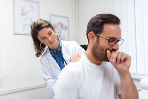 A female doctor at the clinic performs auscultation of the lungs of a patient with symptoms of coronavirus or pneumonia. He is coughing the doctor listens to the wheezing in the lungs photo