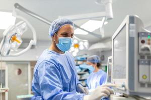 anestesista trabajando en operando teatro vistiendo protector engranaje comprobación monitores mientras sedante paciente antes de quirúrgico procedimiento en hospital foto