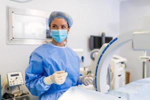hembra cirujano con quirúrgico máscara a operando habitación utilizando 3d imagen guiado cirugía máquina foto