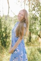 linda joven mujer en un azul vestir sonrisas mientras caminando en el parque foto