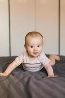 Cute smiling baby boy in bed lying on his belly in bedroom photo