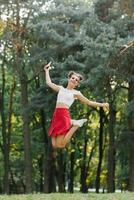 un joven contento mujer en un rojo falda saltos alto en un verano parque, teniendo divertido foto