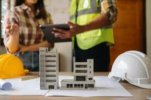 Two colleagues discussing data working and tablet, laptop with on on architectural project at construction site at desk in office photo