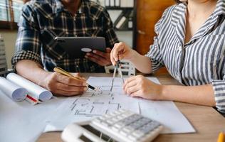 Two colleagues discussing data working and tablet, laptop with on on architectural project at construction site at desk in office photo