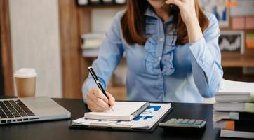 mujer de negocios tiene la alegría de hablar en el teléfono inteligente y escribir en el bloc de notas en la oficina moderna foto