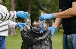 la mano de una mujer recoge desechos plásticos para limpiarlos en una bolsa de reciclaje para limpiarlos en el parque. limpieza, contaminación, concepto de ecología. foto