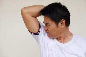 Asian man checks his body odor during he feels hot, raises right arm up, smells his armpit, underarm. Concept , health problem. Unpleasant body odor , smell nasty reaction. Negative emotion. photo