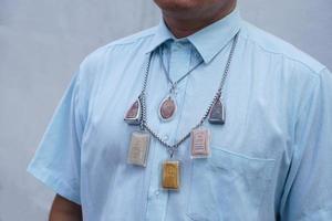 Closeup man in blue shirt wear Thai Buddha amulet necklace. Concept, faith and belief of Buddhist for holy to protect from dangers, bring good luck, business prosperity and wealth. photo