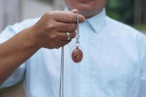 Closeup man in blue shirt holds Thai Buddha amulet necklace.  Concept, faith and belief of Buddhist for holy to protect from dangers, bring good luck, business prosperity and wealth. photo