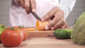 Young man cutting fresh carrots on chopping board on table video