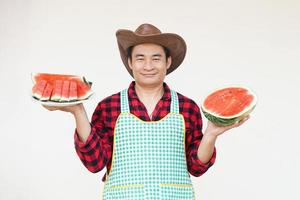 hermoso asiático hombre usa sombrero, delantal, sostiene sandía Fruta a servir y presente. concepto, agricultura cultivos. tailandés agricultor, crecer y vender sandía frutas como económico cultivos. estacional Fruta foto