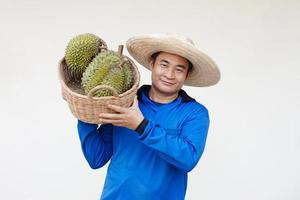 Handsome Asian man farmer wears hat, blue shirt, holds basket of durian fruits. Concept, agriculture occupation.  Thai farmers grow durian fruits as economic and export fruits production photo