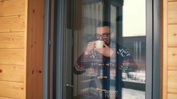 homem bebendo chá ou café perto a janela e olhando através a vidro video