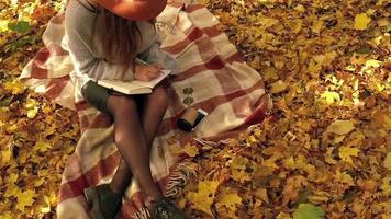 Beautiful woman in a hat and sunglasses is lying on a plaid in an autumn park or forest, resting from the bustle of the city and enjoys good weather. Slow motion video