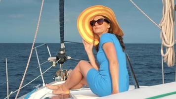 donna nel un' giallo cappello e blu vestito ragazza riposa a bordo un' yacht vicino il faro su estate stagione a oceano video