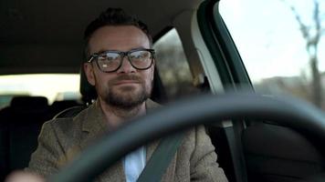 Satisfied bearded man driving a car down the street in sunny weather video