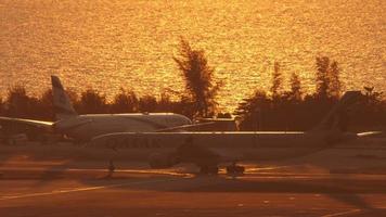 PHUKET, THAILAND FEBRUARY 11, 2023 - Airport in golden backlight. Airplane Airbus A330, A7 AED of Qatar Airways taxiing in glow of sunset. Sea background. Phuket airport. Tourism and travel concept video