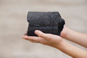 de cerca joven Niños mano sostiene de madera carbón .concepto, aprendizaje a toque y observar en Ciencias tema actividad. naturaleza combustible desde ardiente madera proceso. foto