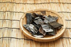 dried Laminaria Kelp Seaweed or kombu slice in wood plate on a Bamboo mat background. dried Laminaria or kelp Seaweed background. konbu, alga, wakame, kombu, kombu photo