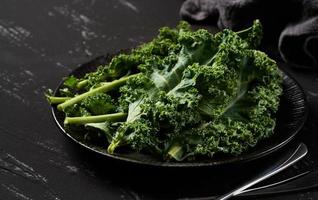 concept of fresh kale leaves salad in a black dish on dark background. green kale leaves salad food in the kitchen. spoon, fork photo