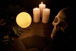 fortune-telling on a wooden table and a white candle with a crystal ball and cards on dark background. predict, prediction, horoscope, macabre, witchcraft, skull photo