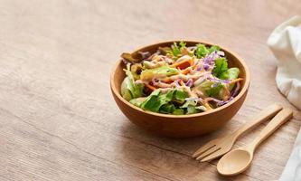 mezcla ensalada desde verde hojas y Cereza tomate en un de madera cuenco con un cuchara y tenedor en blanco madera mesa antecedentes. Copiar espacio foto