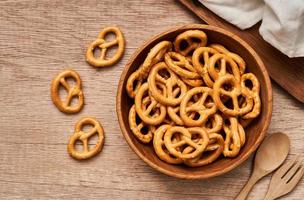 top view or flat lay mini salted pretzel in a wooden bowl with a spoon and fork on wood table overhead background. photo