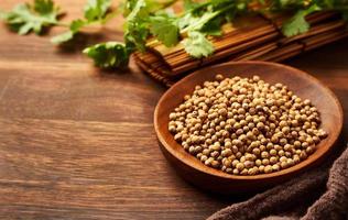 dry coriander seed spice in a wood dish and leaf or leaves on wooden background with copy space photo